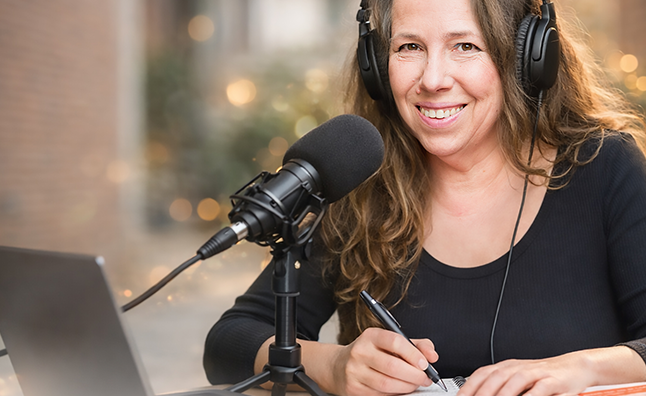 Peggy lächelt wärend sie gerade an ihrem Podcast arbeitet